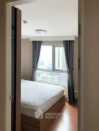 Cozy bedroom with city view, featuring a comfortable bed and large window for natural light.