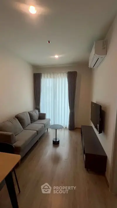 Modern living room with cozy sofa, wall-mounted TV, and natural light from large window.