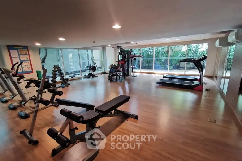 Spacious gym with modern equipment and large windows offering a serene garden view.