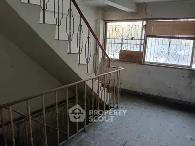 Spacious stairwell in need of renovation with natural light from large window.