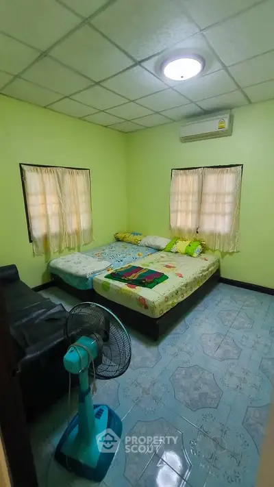 Cozy bedroom with double bed, air conditioning, and fan in a bright green room.
