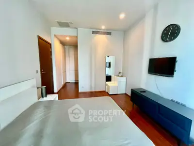 Spacious modern bedroom with sleek furnishings and wall-mounted TV in a stylish apartment.