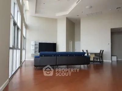 Spacious modern living room with high ceilings and large windows, featuring a sleek sofa and dining area.