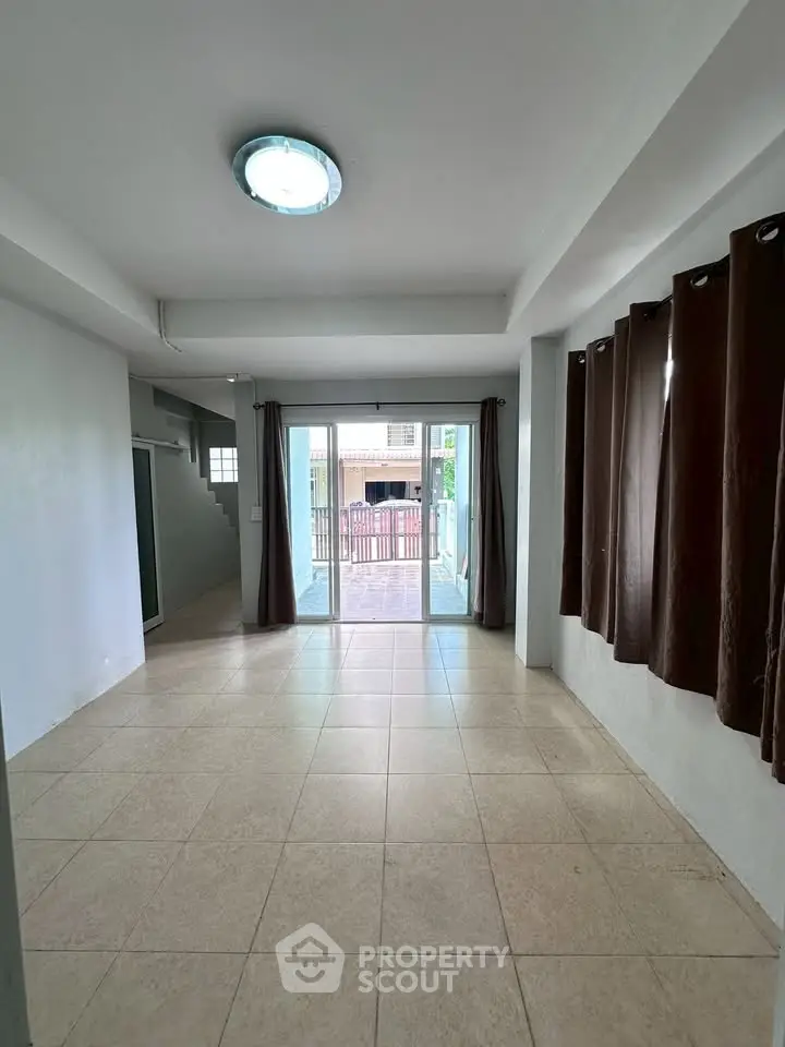 Spacious living room with tiled floor and large windows leading to a balcony.