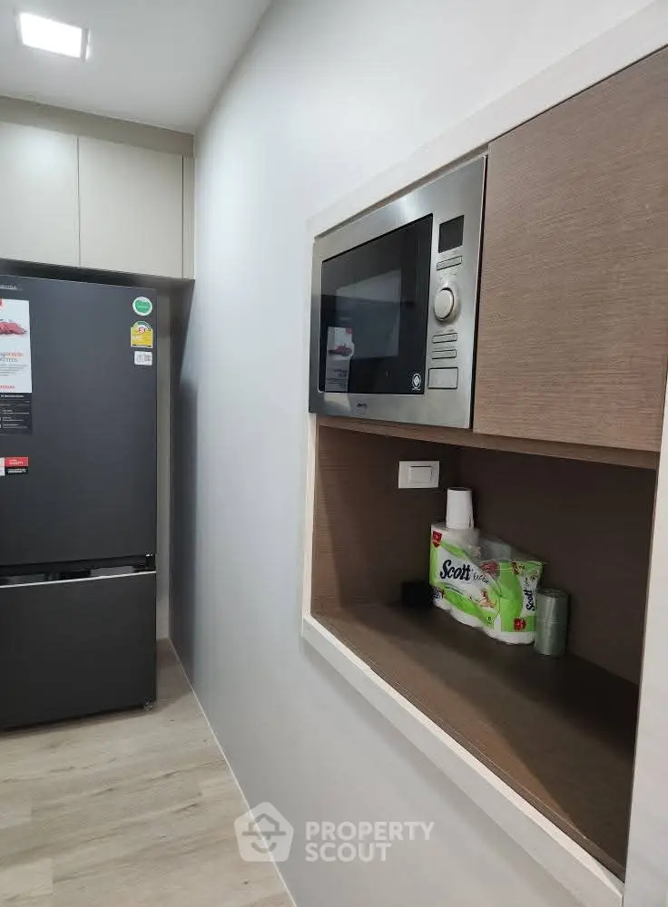 Modern kitchen with built-in microwave and sleek refrigerator, showcasing efficient use of space.