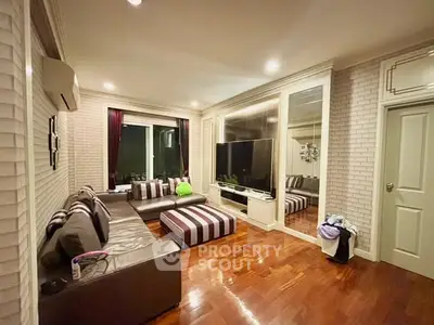 Spacious living room with modern decor and large TV, featuring elegant wooden flooring and stylish furniture.
