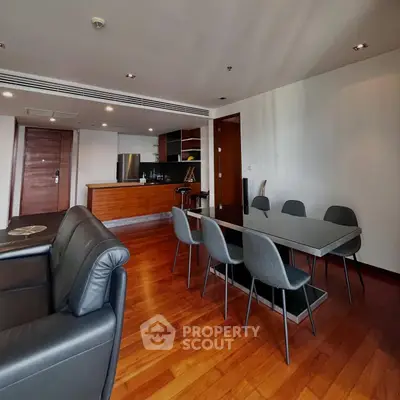 Spacious modern living room with open kitchen and dining area, featuring sleek furniture and wooden flooring.