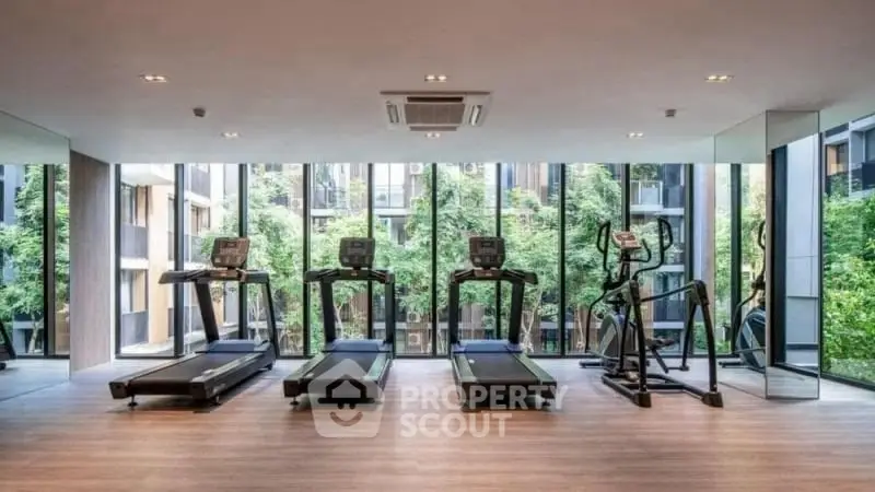 Modern gym with large windows and state-of-the-art equipment in luxury building.