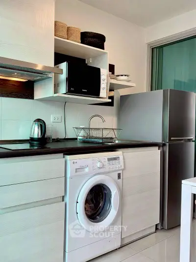 Modern kitchen with washing machine, microwave, and fridge in compact layout.