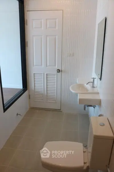 Modern bathroom with white fixtures and tiled walls, featuring a sleek design and ample natural light.
