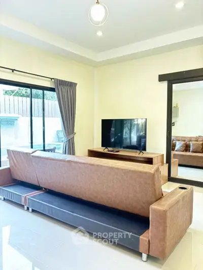 Spacious living room with modern sofa and large TV, featuring natural light from sliding glass doors.