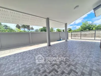 Spacious covered outdoor area with tiled flooring and garden view.