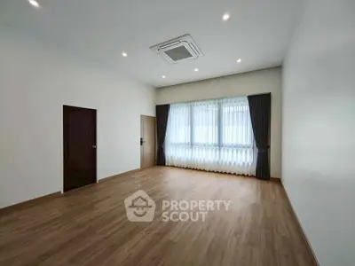Spacious empty room with wooden flooring and large windows, perfect for customization.