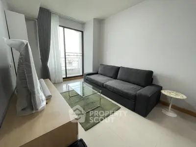 Modern living room with sleek sofa and glass coffee table, featuring a large window with city view.