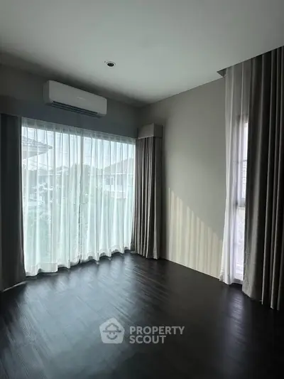 Spacious corner unit with large windows and elegant curtains, featuring sleek dark flooring and modern air conditioning.