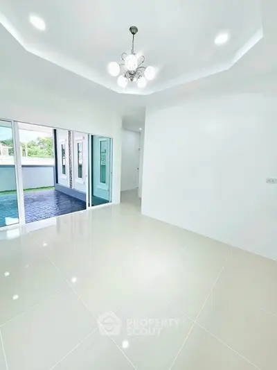 Spacious modern living room with elegant chandelier and large windows opening to a patio.