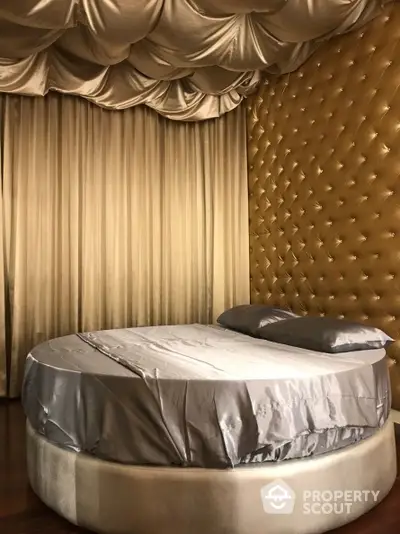 Luxurious round bed with satin sheets in a bedroom with opulent golden tufted wall and matching drapery, exuding elegance and comfort.