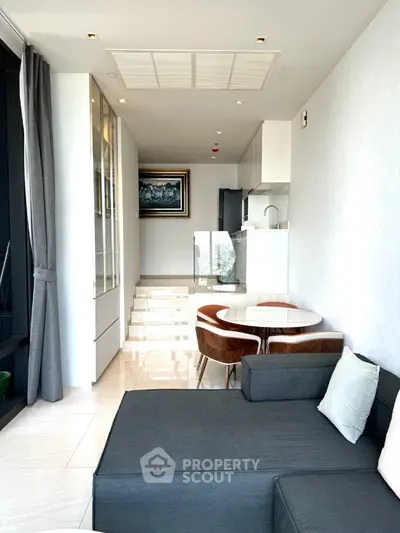 Modern living room with sleek furniture and open kitchen layout, featuring elegant decor and natural light.