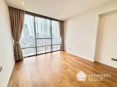 Spacious empty room with wooden flooring and large window offering city views.