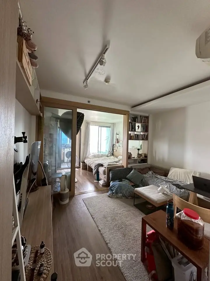 Cozy living room with modern decor and adjacent bedroom, featuring wooden flooring and ample natural light.