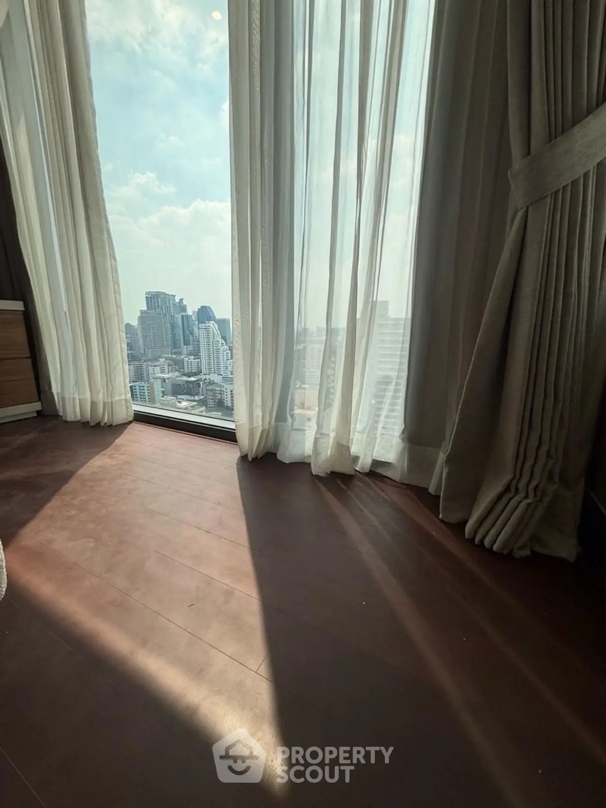 Luxurious high-rise apartment with stunning city view through floor-to-ceiling windows and elegant curtains.