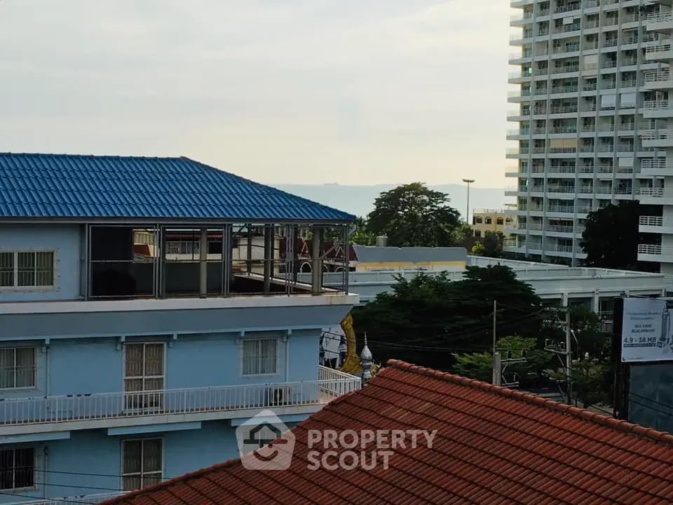 Scenic view of urban buildings with ocean backdrop, showcasing diverse architectural styles and lush greenery.