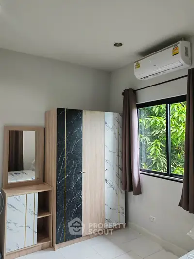 Modern bedroom with stylish wardrobe and air conditioning, featuring a window view of lush greenery.
