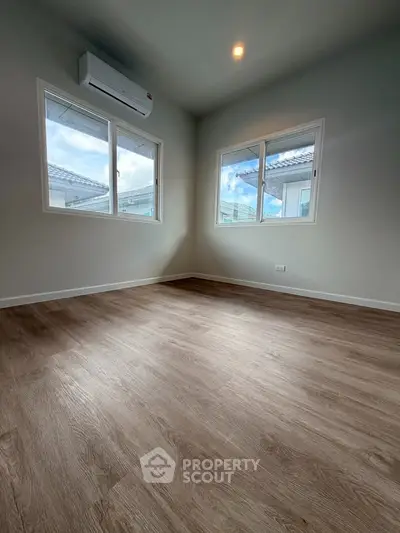 Spacious room with wooden flooring and large windows offering natural light.