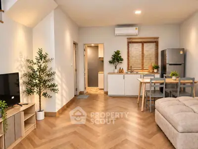 Modern open-plan living room with stylish decor and kitchen area, featuring wooden flooring and natural light.