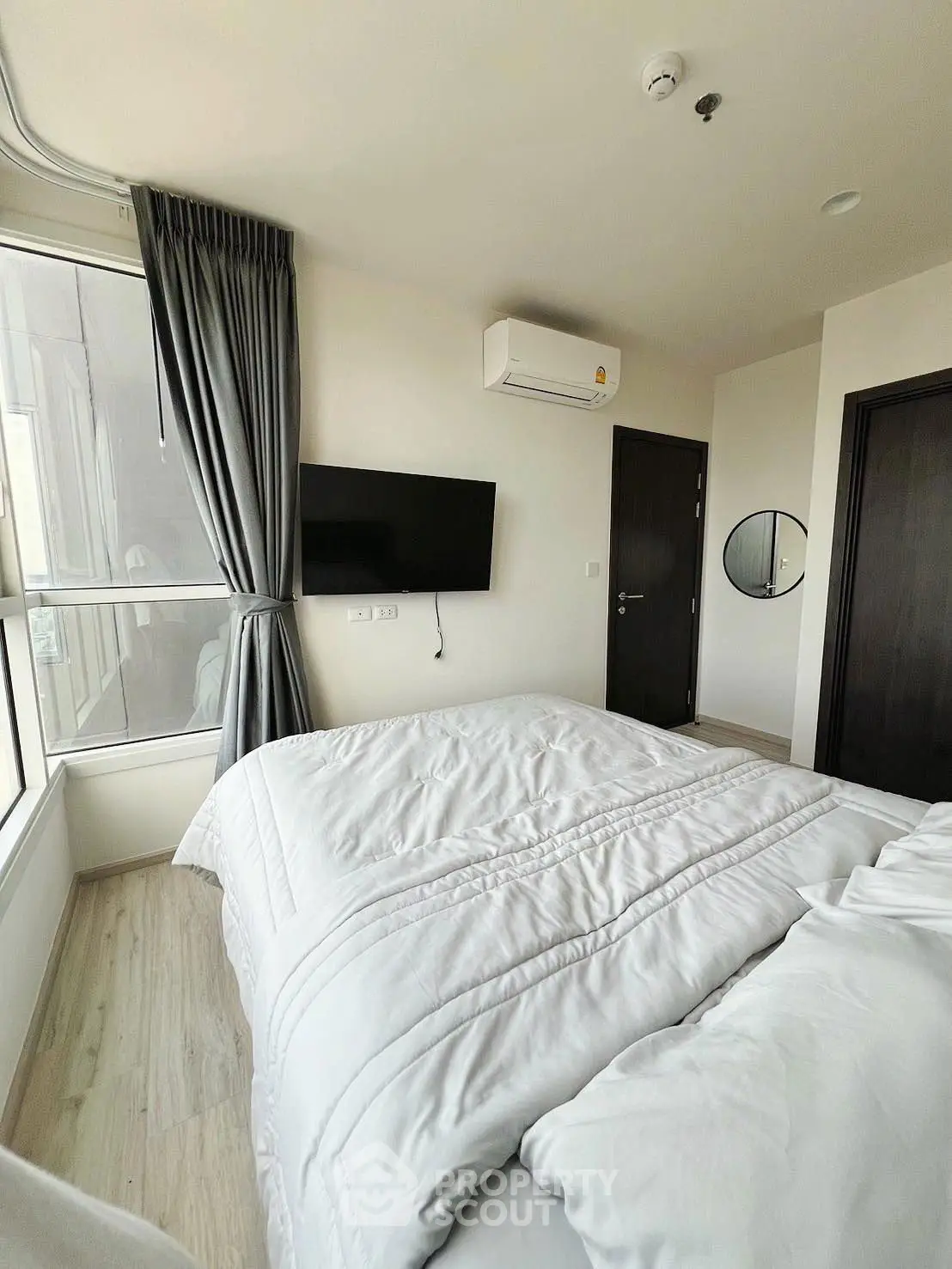 Modern bedroom with cozy bedding and wall-mounted TV, featuring large window and sleek air conditioning unit.