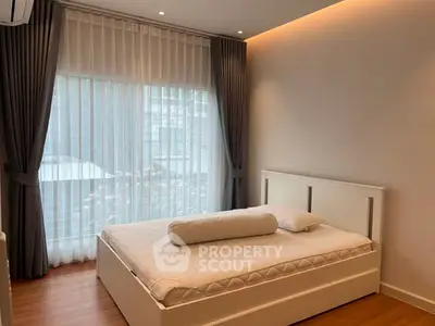 Modern bedroom with elegant curtains and sleek white bed frame in a cozy apartment.