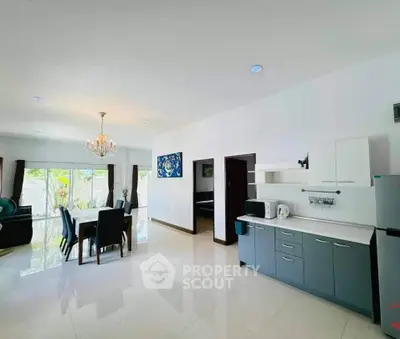 Spacious open-plan living and dining area with modern kitchen, elegant chandelier, and large windows.