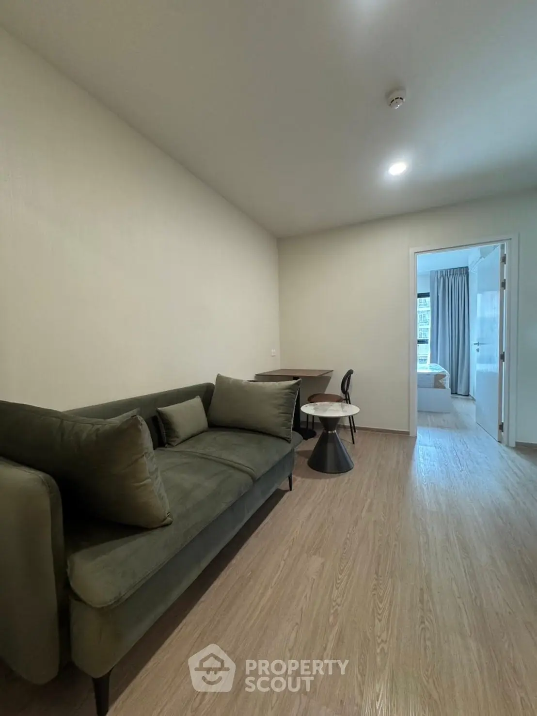 Modern living room with stylish green sofa and wooden flooring, leading to a cozy bedroom.