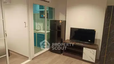 Modern apartment interior with compact kitchen and cozy living area featuring TV and fridge.