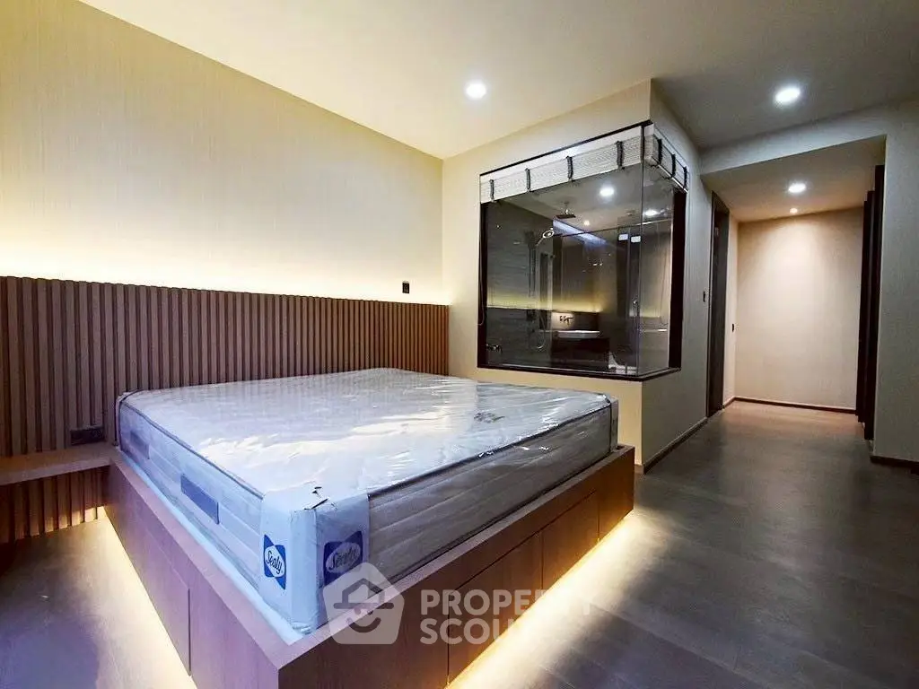 Modern bedroom with sleek design and ambient lighting, featuring a large bed and glass-enclosed bathroom.