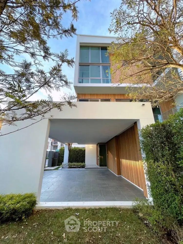 Modern three-story house with sleek design and lush greenery, featuring spacious carport and large windows.