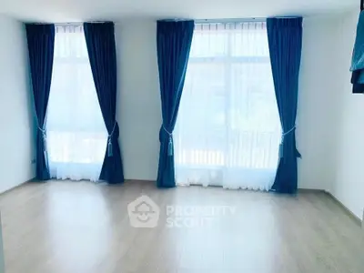 Bright empty room with large windows and blue curtains, perfect for customization.