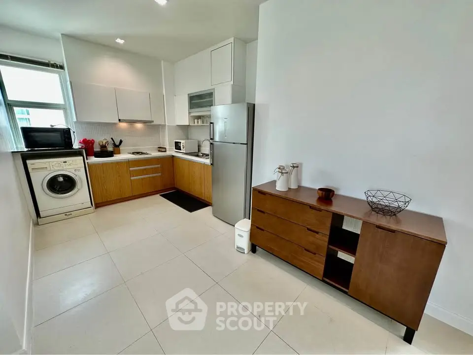Modern kitchen with sleek cabinets, washing machine, and stainless steel fridge in a bright, spacious layout.