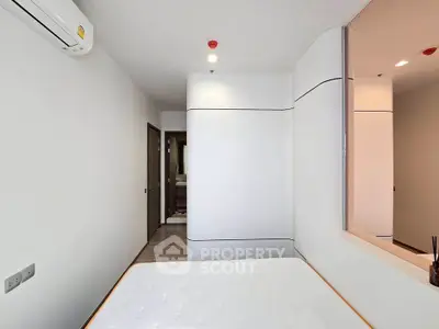 Modern minimalist bedroom with sleek design and white walls, featuring built-in storage and air conditioning.