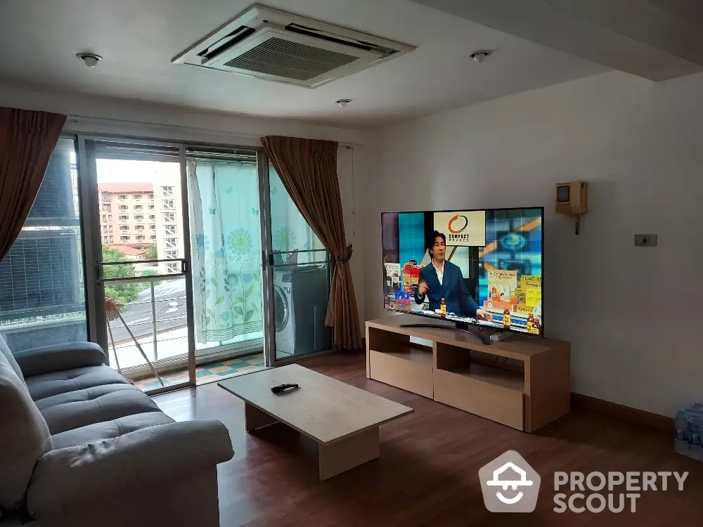 Spacious living room with modern furniture and large TV, featuring a balcony view.