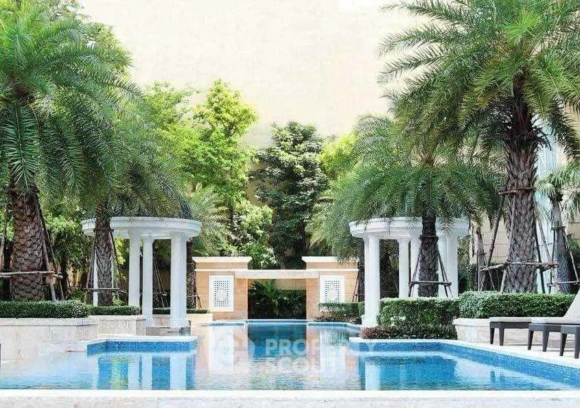 Luxurious outdoor pool area with palm trees and elegant columns in a serene residential setting.