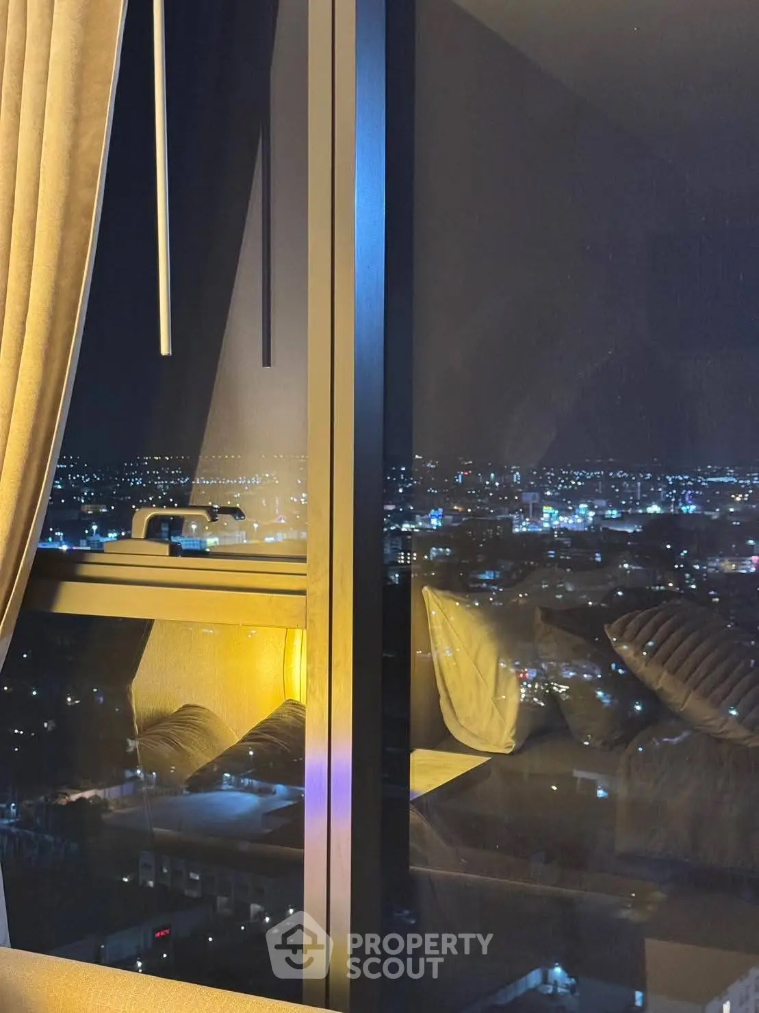 Stunning night city view from a modern apartment window, showcasing urban lights and cozy interior.