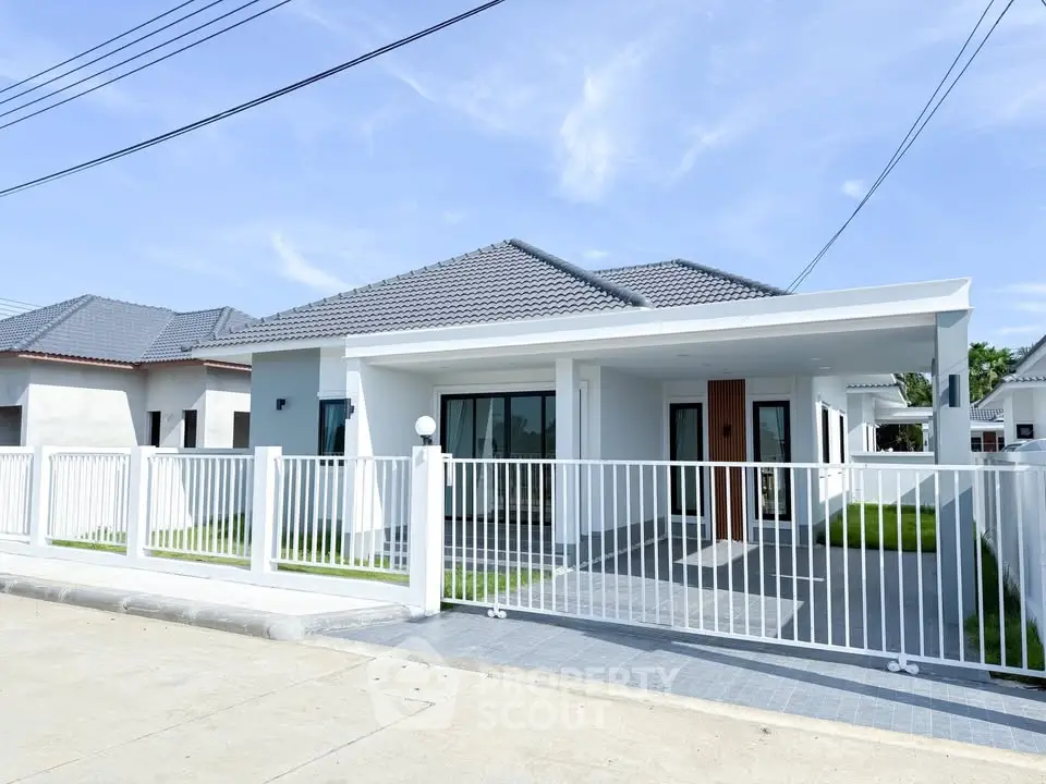 Modern single-story house with white fence and tiled roof in a suburban neighborhood.