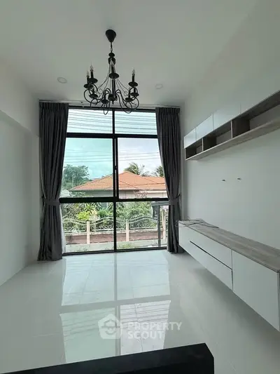 Spacious modern living room with large windows and elegant chandelier, offering a serene view.