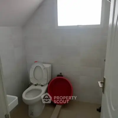 Compact bathroom with white tiles and natural light from window.