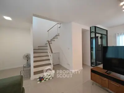 Modern living room with staircase and TV, featuring sleek design and neutral tones.
