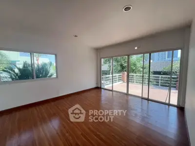Spacious living room with large windows and balcony access, featuring elegant wooden flooring.