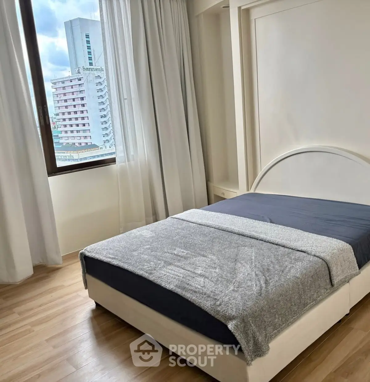 Cozy bedroom with city view, featuring a modern bed and large window for natural light.