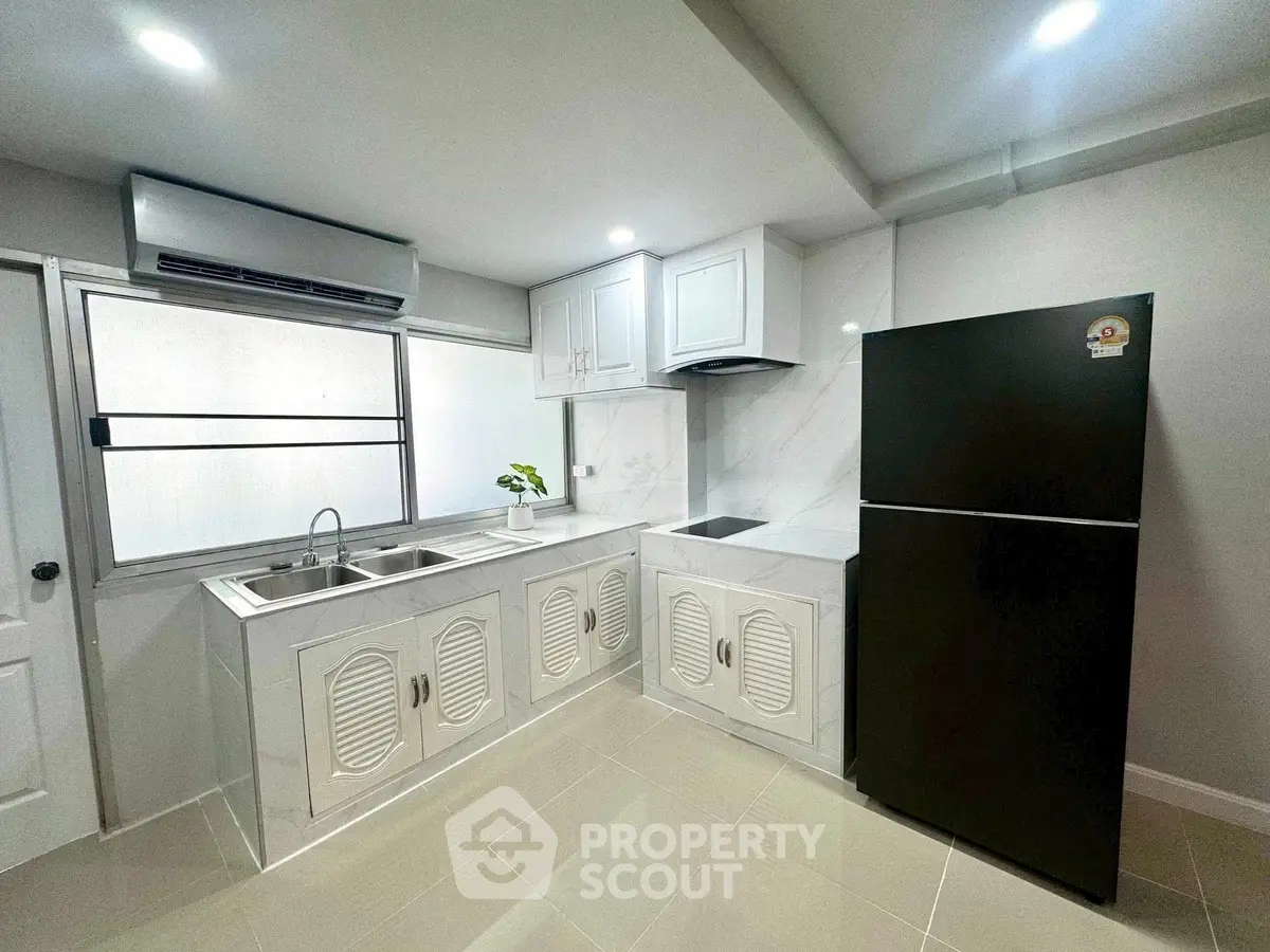Modern kitchen with sleek black fridge and white cabinetry, featuring a dual sink and induction cooktop.