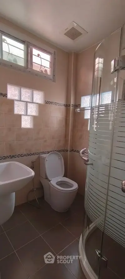 Modern bathroom with glass shower and tiled walls, featuring a sleek design and natural light.